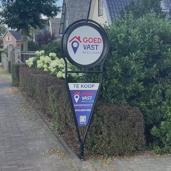 Draaiend makelaarsbord van GoedVast Makelaars die in de tuin staat als Te Koop